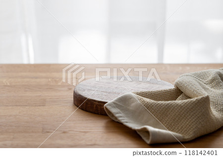 Empty cutting board on wooden texture tabletop with kitchen towel in front of window. Empty cutting board on wooden texture tabletop with kitchen towel in front of window. 118142401