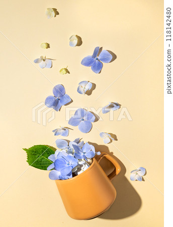 Flat lay bouquet of blue hydrangea flowers falling out of a yellow cup on a yellow background 118142480