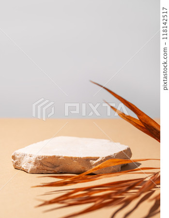 Beige stone slab on a light background with a dry palm leaf and shadow. Beige stone slab on a light background with a dry palm leaf and shadow. 118142517