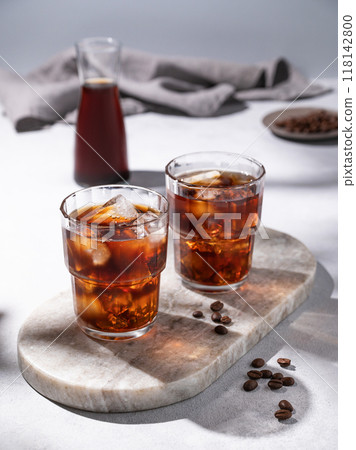 Cold brew coffee in a two glasses with ice on a marble board on a light background with coffee beans Cold brew coffee in a two glasses with ice on a marble board on a light background with coffee beans 118142800