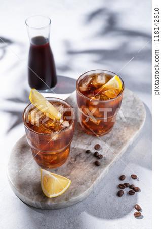 Cold brew coffee in a two glasses with lemon and ice on a marble board on a light background  118142810