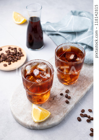 Cold brew coffee in a two glasses with lemon and ice on a marble board on a light background 118142815