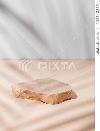Smooth, uneven beige stone slab on a textured light background with a soft shadow from a palm leaf. 118142839