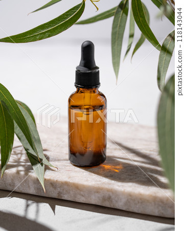 Face and body serum in bottle on a marble board on a white background with green leaves and shadow. 118143044