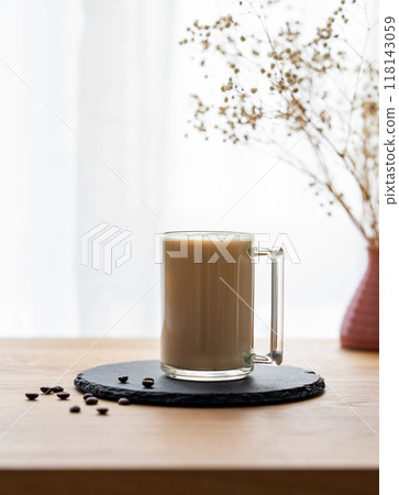 A cup of coffee with milk on a wooden table with coffee beans against the background of a window  A cup of coffee with milk on a wooden table with coffee beans against the background of a window  118143059