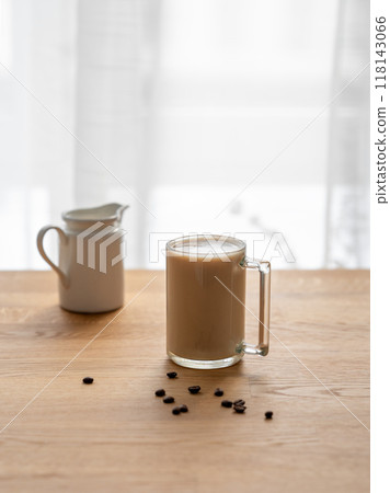 A cup of coffee laltte with milk on a wooden table with coffee beans and milk jug 118143066