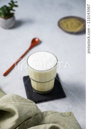 Matcha latte with ice. Green tea with milk in a glass on a light background with spoon, napkin. Matcha latte with ice. Green tea with milk in a glass on a light background with spoon, napkin. 118143067