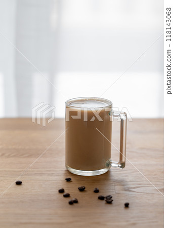 A cup of coffee with milk on a wooden table with coffee beans against the background of a window. A cup of coffee with milk on a wooden table with coffee beans against the background of a window. 118143068