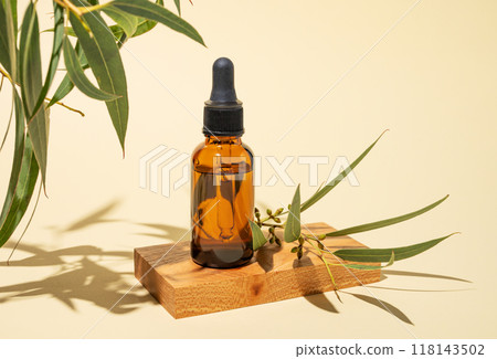 Face and body serum in bottle on a wooden board on a yellow background with green leaves and shadow. Face and body serum in bottle on a wooden board on a yellow background with green leaves and shadow. 118143502