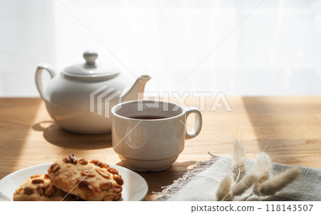 A cup of tea with homemade cookies and a white teapot on a wooden table against the background  118143507