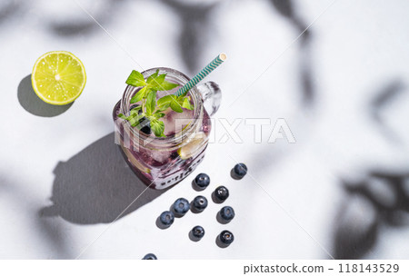 Blueberry mojito or lemonade with lime, ice and mint in a glass on a light background with berries Blueberry mojito or lemonade with lime, ice and mint in a glass on a light background with berries 118143529