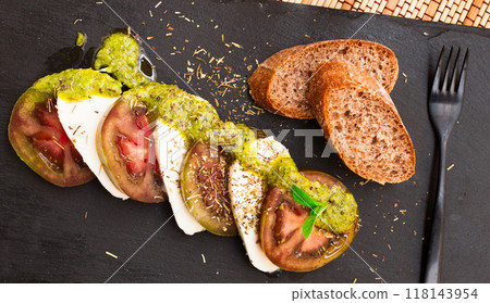 Caprese salad with mozzarella, black tomatoes and pesto on black stone plate 118143954