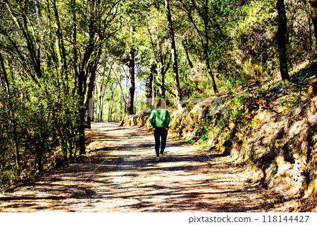 Blonde woman with curly hair walking along the path of trees and leaves in autumn in the Montseny Natural Park in Barcelona 118144427