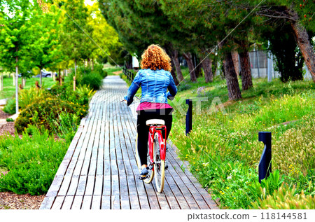 Blond woman walking in the park with a blue denim on a red bicycle Blond woman walking in the park with a blue denim on a red bicycle 118144581