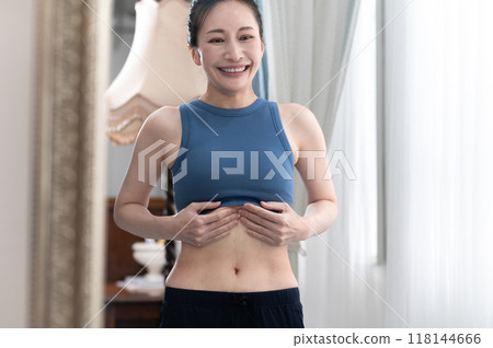 A woman in sportswear worries about her figure in front of a mirror A woman in sportswear worries about her figure in front of a mirror 118144666