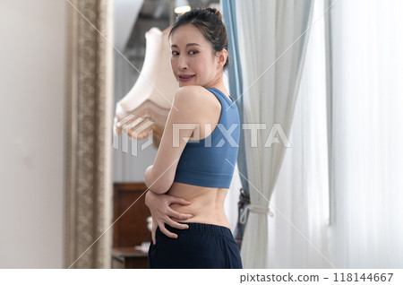 A woman in sportswear worries about her figure in front of a mirror A woman in sportswear worries about her figure in front of a mirror 118144667