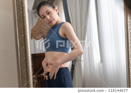 A woman in sportswear worries about her figure in front of a mirror 118144677