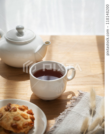 A cup of tea with homemade cookies and a white teapot on a wooden table against the background 118148200