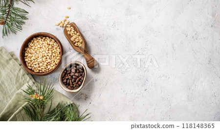 Pine nuts in a bowl and wooden scoop on a napkin on a light texture background with branches Pine nuts in a bowl and wooden scoop on a napkin on a light texture background with branches 118148365