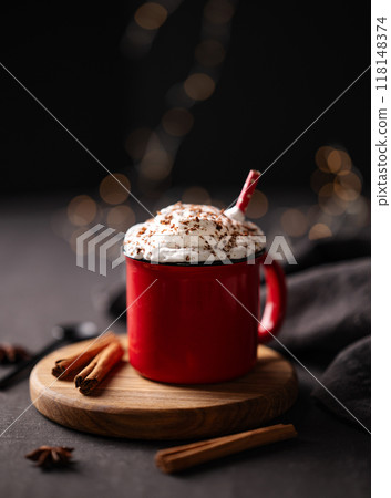 Red mug with hot chocolate or cocoa with whipped cream on a wooden stand with cinnamon sticks Red mug with hot chocolate or cocoa with whipped cream on a wooden stand with cinnamon sticks 118148374
