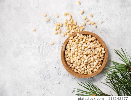 Pine nuts in a  wooden plate and scattered on a light texture background with branches  118148377