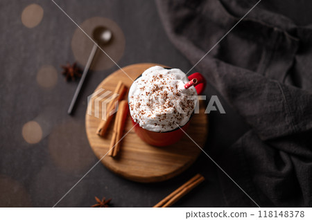 Red mug with hot chocolate or cocoa with whipped cream on a wooden stand with cinnamon sticks  118148378