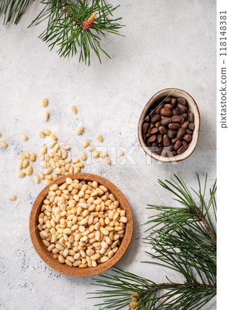 Pine nuts in a bowl and scattered on a white texture background with branches of pine needles. Pine nuts in a bowl and scattered on a white texture background with branches of pine needles. 118148381