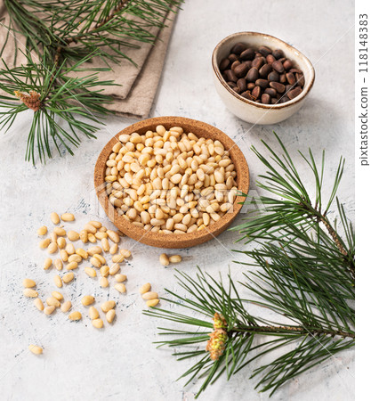 Pine nuts in a bowl  and scattered on a white texture background with branches of pine needles. 118148383