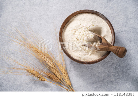 Natural wheat flour in a wooden bowl on a blue background with branches of wheat. Natural wheat flour in a wooden bowl on a blue background with branches of wheat. 118148395