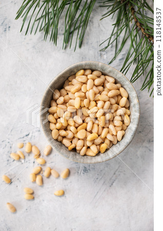 Pine nuts in a bowl  and scattered on a white texture background with branches of pine needles 118148537