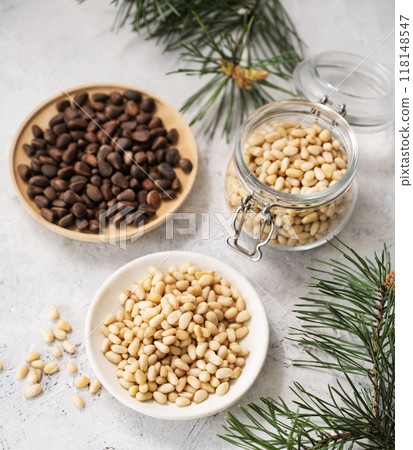 Pine nuts in a white plate and a jar on a light texture background with branches of pine needles Pine nuts in a white plate and a jar on a light texture background with branches of pine needles 118148547