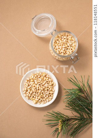 Pine nuts in a bowl and jar on a yellow background with branches of pine needles. 118148551