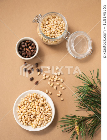 Pine nuts in a bowl and jar on a yellow background with branches of pine needles.  118148555