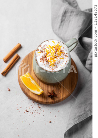 Mug of hot chocolate with whipped cream and orange zest on a wooden board on a light  background 118148572