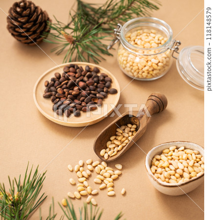 Pine nuts in a bowl and scoop on a yellow background with branches of pine needles. 118148579