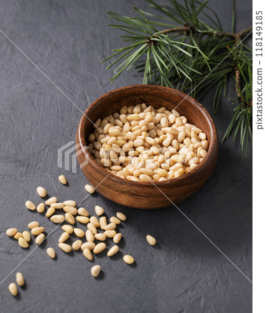 Pine nuts in a wooden bowl and scattered on a dark background with branches of pine needles Pine nuts in a wooden bowl and scattered on a dark background with branches of pine needles 118149185