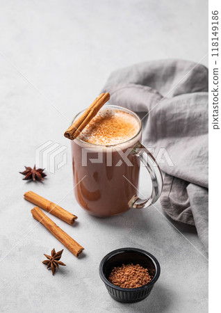 Glass mug with hot chocolate and milk foam on a light background with cinnamon sticks Glass mug with hot chocolate and milk foam on a light background with cinnamon sticks 118149186