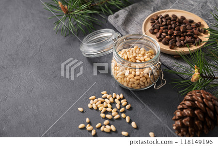 Pine nuts in a jar, bowl and a scattered on a dark background with branches of pine needles and cone Pine nuts in a jar, bowl and a scattered on a dark background with branches of pine needles and cone 118149196