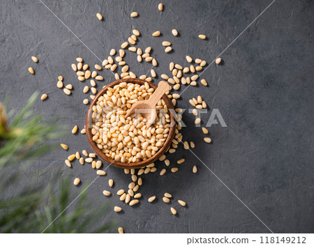 Pine nuts in a bowl and a scattered on a dark background with branches of pine needles. Pine nuts in a bowl and a scattered on a dark background with branches of pine needles. 118149212