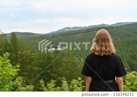 View from the back of young hiker girl wearing backpack and beanie hat standing on edge of cliff and enjoying landscape, sunset, mountains and clouds. 118149231