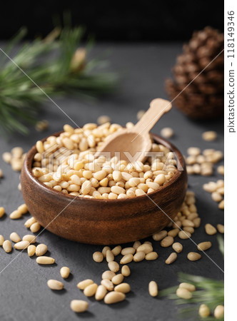Pine nuts in a bowl with a scoop on a gray background with a branch of pine needles close up. Pine nuts in a bowl with a scoop on a gray background with a branch of pine needles close up. 118149346