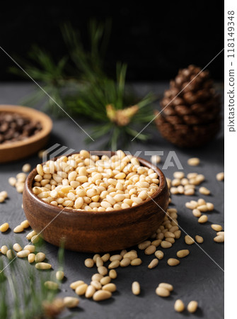 Pine nuts in a bowl and a handful of unpeeled nuts on a gray background with a branch  118149348