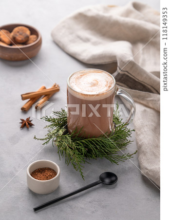 Glass mug of hot chocolate with whipped cream on a stand with pine branches on a light background Glass mug of hot chocolate with whipped cream on a stand with pine branches on a light background 118149353