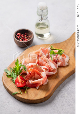 Snack wooden board with bacon or prosciutto on a light background with spices, tomatoes and herbs. 118149369