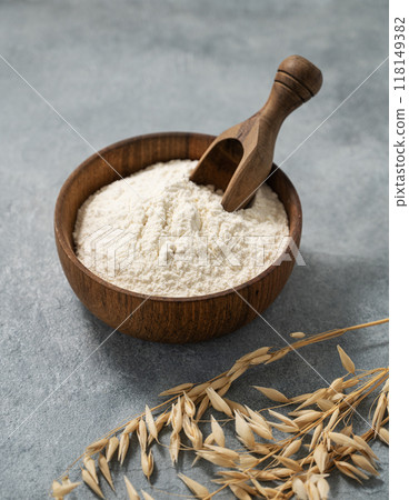 Oatmeal in a wooden bowl with a scoop on a blue background with branches of dry oats. Oatmeal in a wooden bowl with a scoop on a blue background with branches of dry oats. 118149382