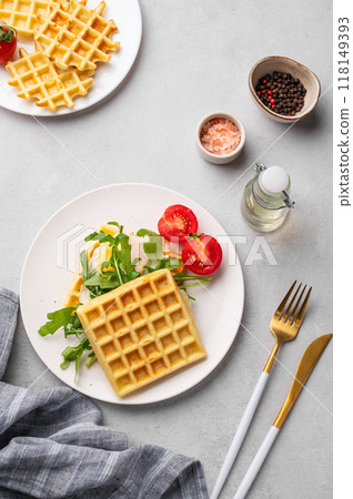 Waffles with fried egg, cherry tomatoes and arugula on a white plate on a gray texture background Waffles with fried egg, cherry tomatoes and arugula on a white plate on a gray texture background 118149393
