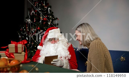 Santa Claus taking notes from a young woman near Christmas tree. Santa Claus taking notes from a young woman near Christmas tree. 118149950