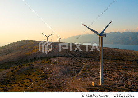 Wind turbines generate eco-friendly power on Pag Island, encircled by the Adriatic Sea at sunset.  118152595