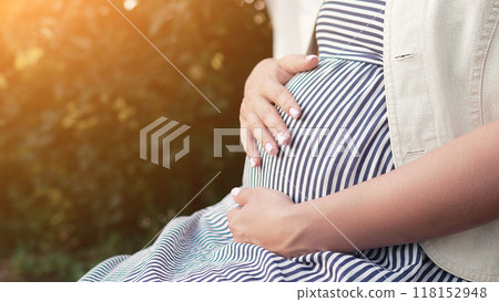 Pregnant woman sitting in summer home garden. Future mom caressing belly bump, green nature background. Expectant mother in summer dress, happy motherhood. Pregnant woman sitting in summer home garden. Future mom caressing belly bump, green nature background. Expectant mother in summer dress, happy motherhood. 118152948