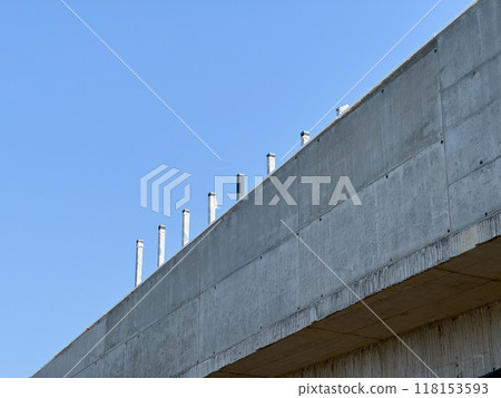 A section of a concrete building with visible posts protruding from the roof against a clear blue sky 118153593